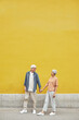 © Seventyfour - Pop color full length portrait of modern senior couple holding hands outdoors while walking against yellow background, copy space