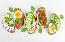 Five Bread Toasts With Vegetables, Egg And Basil On A Light Concrete Table