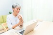 © 聆慈 林 - Senior asian woman at phone works on her laptop at home.