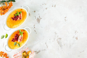 Two creme brulee desserts with fresh figs and currants on a white stone table in an autumn composition, copy space.