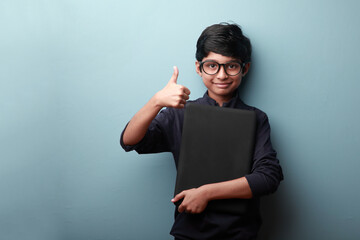 Canvas Print - Portrait of a happy boy holding a laptop and showing thumbs up