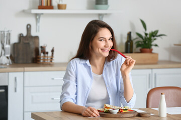 Beautiful young woman eating tasty quesadilla at home