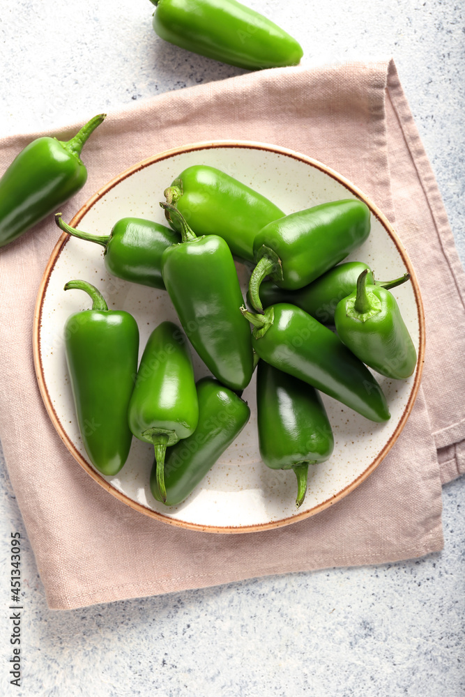 Plate with green jalapeno peppers on light background