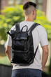 Rear view man walking in city with black leather backpack