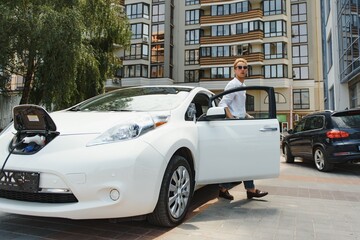 portrait of young handsome man in casual wear, standing at the charging station. Eco electric car concept