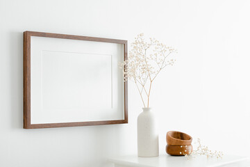 Horizontal wooden frame mockup with copy space for artwork, photo or print presentation. White wall with furniture and dry gypsophila plant.