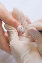 Wall Mural - Manicurist drawing on female nails. Nail beautician making a draw on clients nails in beauty salon. Woman in nail salon receiving manicure by beautician, close up. Shallow depth of field