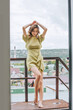 © kuzmichstudio - Young model girl in a dress is standing on the balcony against the background of a city and the sky