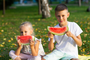 Wall Mural - To cute kids lttle boy and girl eating juicy watermelon in the picnic at autumn park meadow.