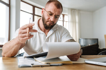 Wall Mural - White man in eyeglasses writing down notes on clipboard while working