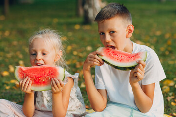 Wall Mural - To cute kids lttle boy and girl eating juicy watermelon in the autumn park meadow.