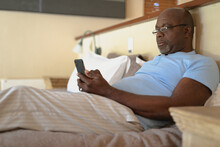 Senior African American Man Laying In The Bad And Using Smartphone