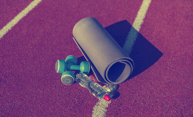 Wall Mural - Training equipment on the stadium track. Mat, dumbbells and a bottle of water. Outdoor workout