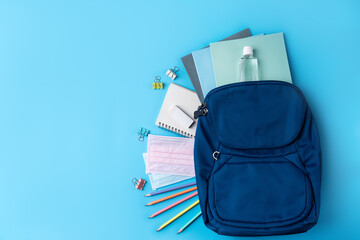 Blue backpack with stationery over blue table background.