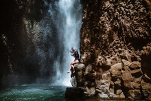 Woman Sitting On Rock Near Waterfall