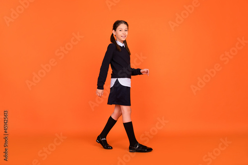 Full size photo of cheerful positive happy little girl walk classes good mood smile isolated on orange color background