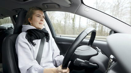 Wall Mural - Young woman with natural look driving a passenger car on a German highway. The young woman shows various emotional reactions to the traffic event.