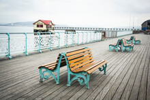 A Wooden Bench On The Old Pier With Old Lifeboat Station On The Background. Swansea, South Wales, UK