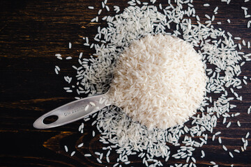 An Overflowing Measuring Cup of Uncooked Long Grain Rice: A stainless steel measuring cup filled with raw white rice grains