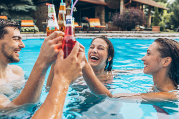 Wall Mural - Group of young people refreshing in a swimming pool and toasting together with a cold drink.	