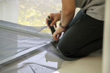 Wall Mural - man install mosquito net wire screen on house window protection against insect