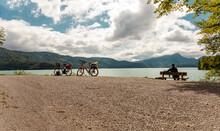Cycling, Rear View Of A Biker Sitting On A Bench For Relaxation In Green Idyllic Landscape Scenery. Beautiful Bavarian Panorama Of Lake Walchensee. Upper Bavaria Germany. Europe Bavarian Prealps