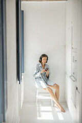 Wall Mural - Young woman enjoys music in headphones while sitting alone in a bright room at home. Self-isolation and loneliness concept