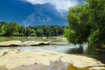 a stunning shot of the silky brown waters of the Chattahoochee river with vast miles of lush green trees along the river with blue sky and clouds at McIntosh Reserve Park in Whitesburg Georgia