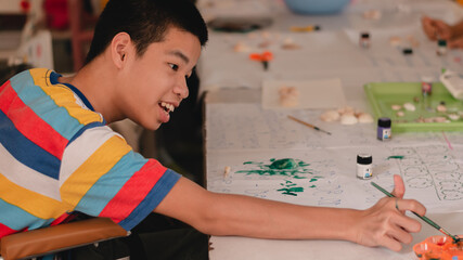 Handicapped teenager boy on wheelchair with happy face doing art work with friends, Lifestyle of smart disabled kid learning activity in special children school, Mental health classroom concept.