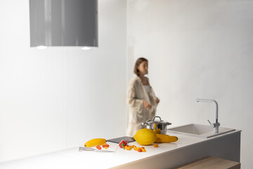 Wall Mural - Woman cooking vegetarian food from fresh yellow vegetables, looking at the recipe on a digital tablet at modern kitchen