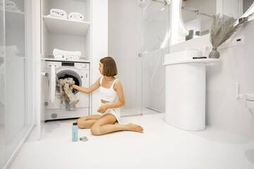 Wall Mural - Woman loading dirty clothes into the washing machine in white bathroom