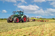 A Tractor with hay tedder turning the grass cuttings in the meadow