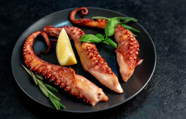 Wall Mural - grilled octopus tentacles, on a dark plate on a stone background