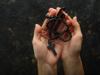 In women's hands, a crucifix and a rosary. Minimalism. Dark background. Religion, faith, Catholicism, prayer, meditation. Poster, banner, advertisement.