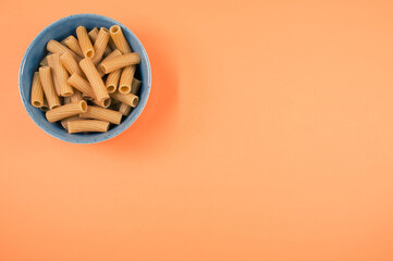 Wall Mural - Top view of uncooked rigatoni pasta on a bowl isolated on an orange background