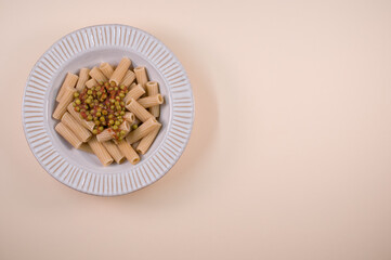 Poster - Top view of rigatoni pasta with green peas on a plate isolated on brown background