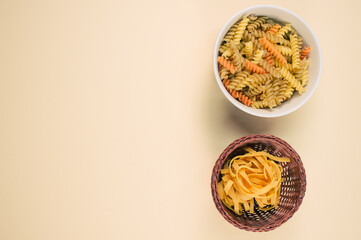 Wall Mural - Top view of tri-color rotini and fettuccine pasta on a bowl isolated on brown background