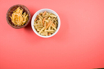 Wall Mural - Top view of uncooked tri-color rotini and fettuccine pasta on a bowl isolated on pink background