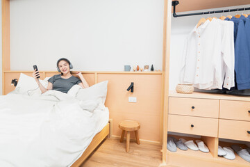 Wall Mural - Bedroom concept on the comfortable bed a girl listening her favorite songs by wearing a headphone in the morning