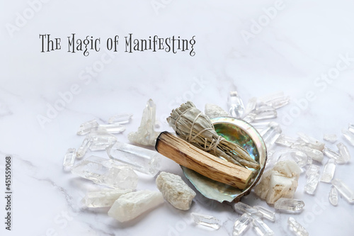 The Magic of Manifesting - motivation quote. Clear quartz minerals, palo santo, sage bundle on marble background. gemstones crystals for healing esoteric spiritual practice, relaxation, meditation