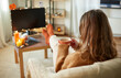 © Syda Productions - halloween, holidays and leisure concept - young woman watching tv and drinking hot chocolate with her feet on table at cozy home