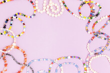 Necklaces And Bracelets Made From Beads And Pearls On A Purple Background. Border Frame With Copyspace.