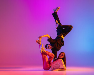 Two young people, guy and girl in casual clothes dancing contemporary dance, hip-hop over pink background in neon light.