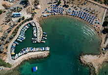 Aerial Drone View Of Beach With People Swimming And Fishing Boats Moored At The Harbor. Protaras Paralimni Cyprus