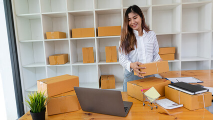 Startup, small business, SME, owner of Asian female entrepreneurs working with boxes. Smile and check the sales deficit using a computer. After she succeeded in thinking differently in online SME busi