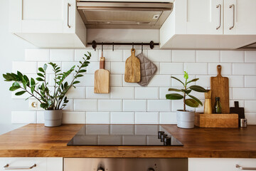 Kitchen brass utensils, chef accessories. Hanging kitchen with white tiles wall and wood tabletop.Green plant on kitchen background