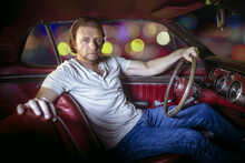 Man In Vintage Classic Car With Red Interior And Wooden Steering Wheel At Night 