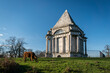 A highland cow grazing in front of Darnley Mausoleum, a restored 18th century mausoleum set in peaceful public woodland. in Kent, UK