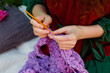 Selective focus. Close-up crochet. Women's hands are knitting a lilac openwork shawl.
