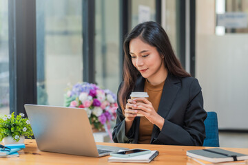 Wall Mural - Young Asian businesswoman sitting at the office holding a coffee cup.